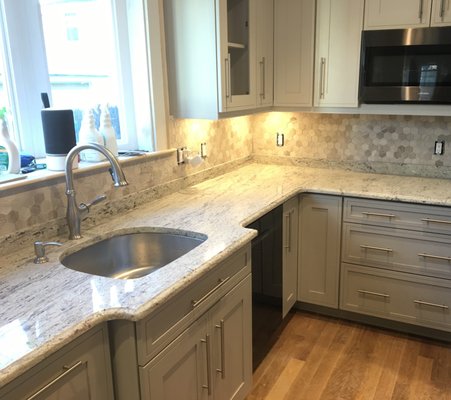 Two tone grey cabinetry with hexagon shaped porcelain tiled backsplash and granite countertops.