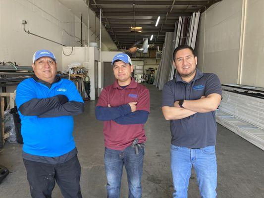 A picture of the crew at Unlimited Garage Door Services standing in their building with panels for garage doors behind them