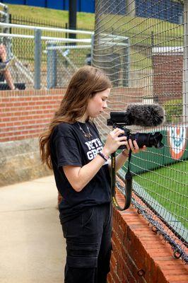 Emma is taking pictures and videos at a softball game for the University of North Georgia Athletics.