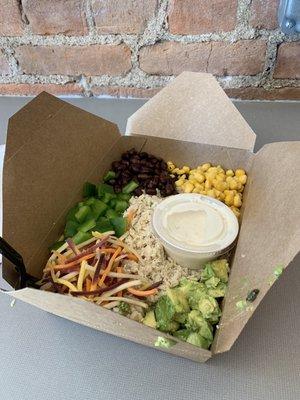 Bowl with rice, chicken, corn, black beans, avocado, carrots, green pepper, and vegan ranch.