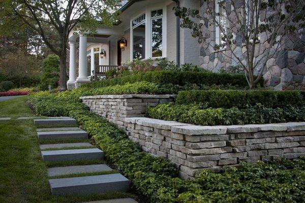 Here is a sturdy retaining wall, adorned with small bushes, trees, & vibrant ground cover plants.