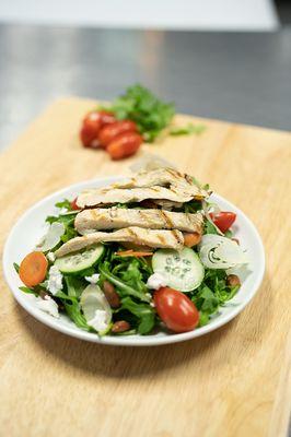 Grilled chicken arugula salad with baby tomatoes, goat cheese, cucumbers and side of balsamic vinegar