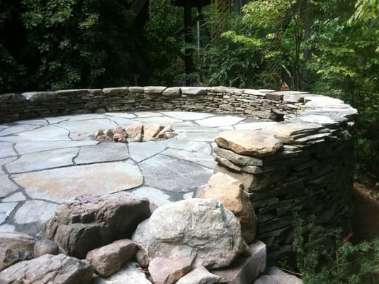 A three foot dryset retaining wall with a two foot freestanding seat wall on top, surroumds a rustic patio and a firepit