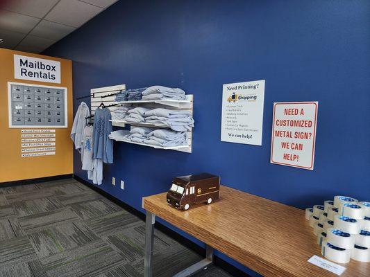 Promotional items shelf, table with pyramid of tape, UPS truck, and commercial mailboxes.