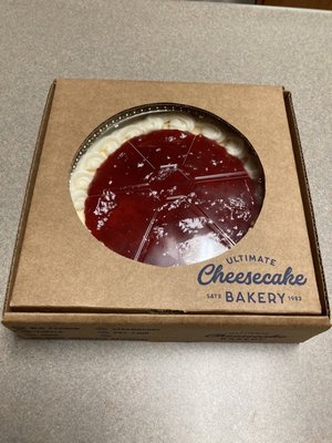 Medium cheesecake with strawberry topping, given in a cardboard box.