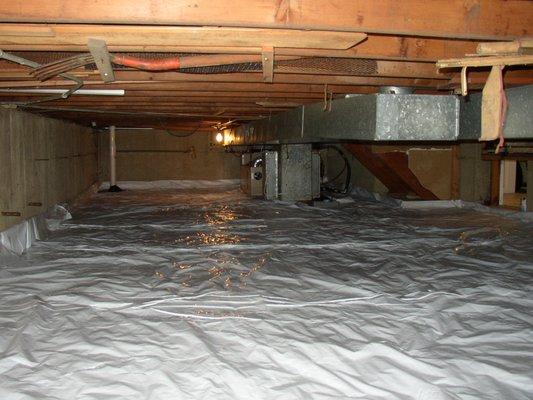 Low crawlspace covered with vapor barrier.