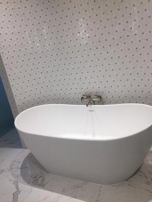 Standing deep tub with tiled wall.