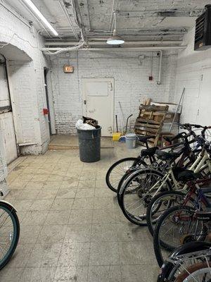 Haunting bike room guarded by trash can.