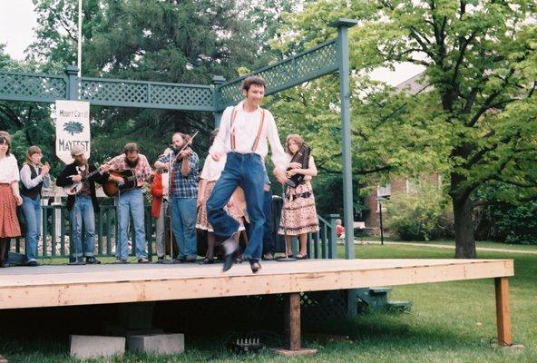 Clogger performing a buck dance.  Members of Stone Soup can be seen playing  bones, banjo, guitar, fiddle, and zither.