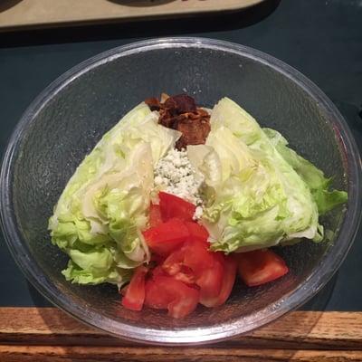 Two wedges of Iceberg lettuce with blue cheese, tomatoes and bacon.