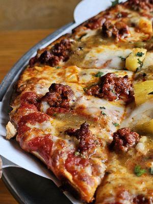 Close-up of The Weird Al Pastor Tavern Pizza with Chorizo Pork, Salsa Verde, Cilantro, Tajin Dusted Pineapple, Mozzarella, Cali Red Sauce.