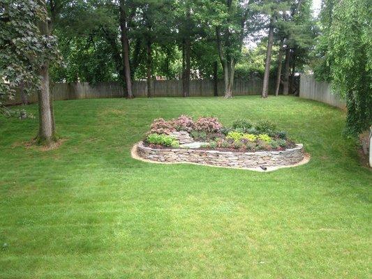 Backyard garden incorporating a stacked stone wall, beautiful plantings and a small pond