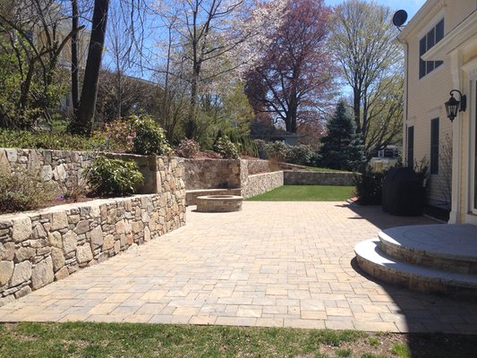 Patio made with pavers and a stone wall. Steps are made with stone and granite.