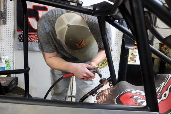 A student in the high performance program grinding on a sprint car frame.