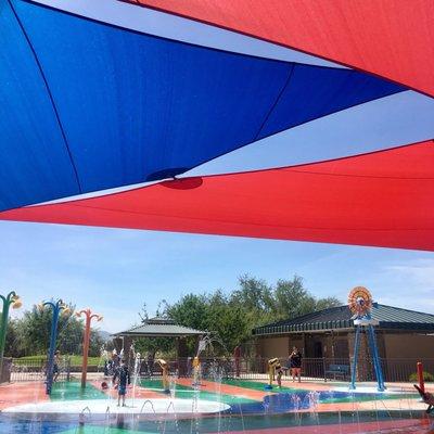 Shade sails, splash pad, ramada, grass off to the left and bathroom right of ramada