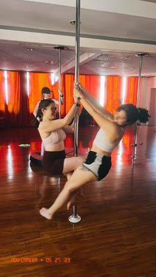 Two friends learning how to spin on the pole together in Shakira's pole 1 class