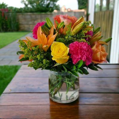 Sunset Passion - Low arrangement with Orange lilies, yellow and orange roses, hot pink carnations, yellow solidago and greenery.