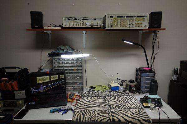 Work area, equipment includes Panasonic VP-7722 audio analyzer, Panasonic VP-8175 FM signal gen, Weller soldering iron and many other things