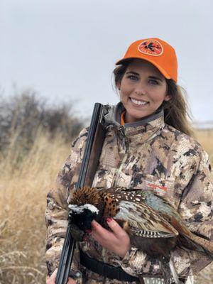 A female hunter holds her downed pheasant in a field near Yellowstone International Airport.