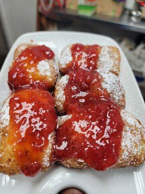 Beignets covered in powdered sugar with a sweet yet subtle strawberry topping