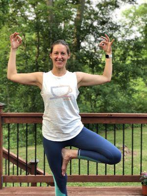 Yoga practitioner doing tree pose with cactus arms with woods in the background.