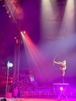 Balancing contortionist woman using a bow and arrow with her feet