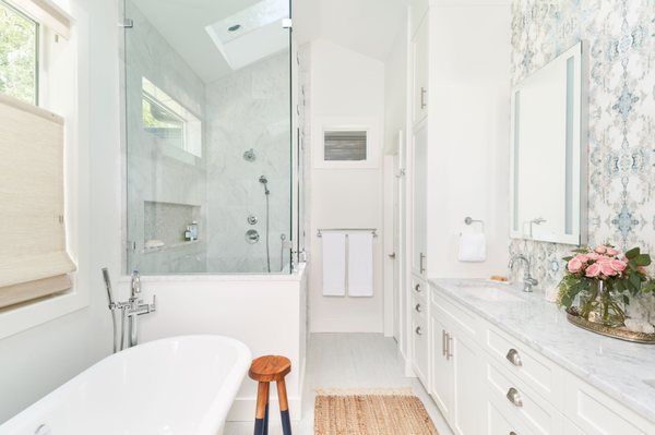 Vaulted master bath with marble vanity, wallpaper, and freestanding tub