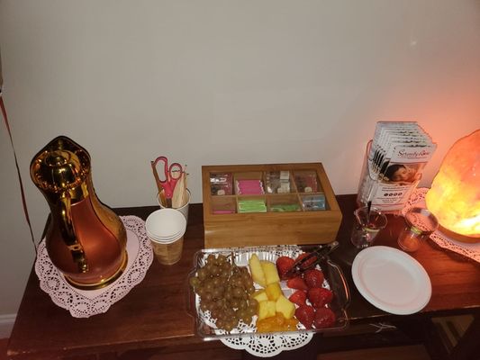 Table setting with selection of teas, hot water container, and fruit tray.