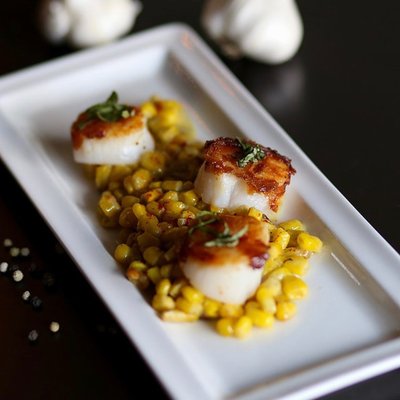 Seared sea scallops served over scallion cream corn and topped with tomato jam and herb salt