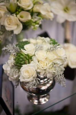 Elegant white roses, silvery grey dusty miller, fragrant white freesia and unique succulents create a charming centerpiece.