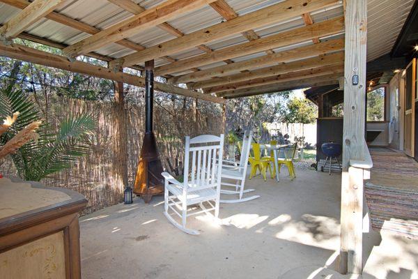 Private covered backyard with rocking chairs, dining table, chimenya and stock tank fountain.