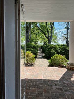 A view from inside the house looking outside. There is seating on either side of the house on the patio, as well as in the green area.