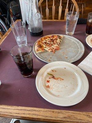 Mostly eaten pizza with bacon and spinach toppings, along with a carafe of soda.