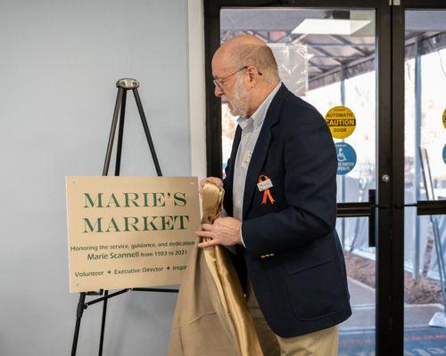 Board President, Gordon White III reveals sign naming the self-serve client market after Marie Scannell, the Exec. Dir. for over 30+ years.