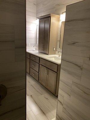 View from walk in shower, showing the double sinks, tile walls and floors.