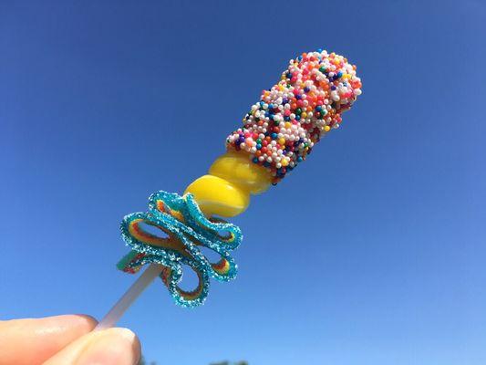 Candy fun! Banana lollipop dipped in chocolate, sprinkled with non-pareils and a rainbow sour belt!