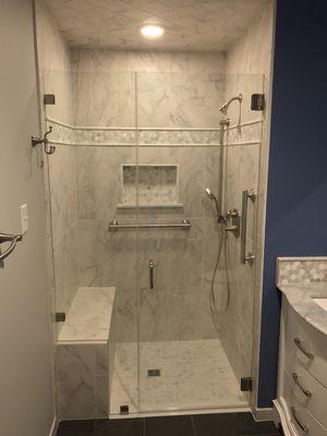 A Walk in shower with frameless glass enclosure, tile bench seat and recessed soap and shampoo niche