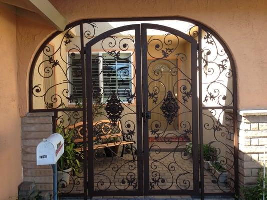 Custom wrought iron entry enclosure with handforged scrollwork. This open concept design is striking and secure. Rustic brown.