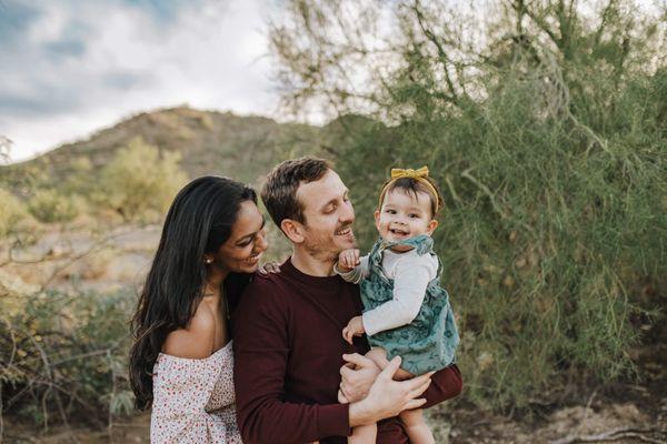 A beautiful family of three celebrating baby girl's first birthday with a desert background