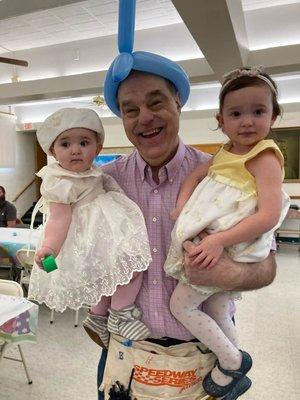 Pastor Bill at our annual Easter Egg hunt holding his granddaughters and sporting his balloon twisting gear.