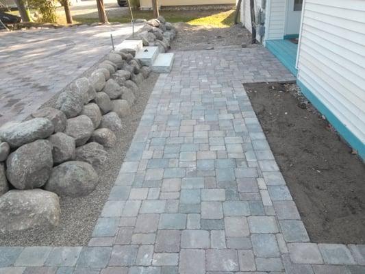 A raised brick paver driveway on the left to promote water drainage away from the house and a wrap around walkway approaching the entrance.