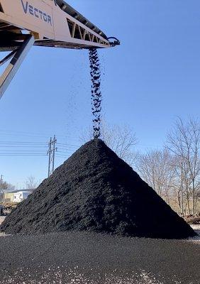 Premium dyed black mulch exiting a conveyer belt into a large pile.