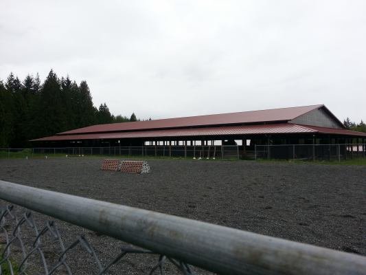 View over the outdoor sand and rubber footing arena to the covered sand and rubber footing arena.