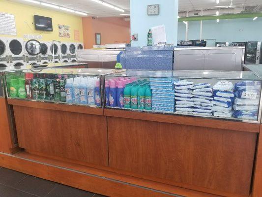 Laundry cleaning products are displayed for sale for our client's convenience, and they include liquid and powder soap, bleach and sotners.