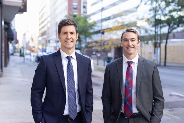 Two businessmen in suits pose confidently on a Cincinnati city street, captured for their personal branding headshots by our photography stu