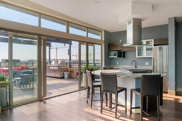 Resident kitchen with island and granite countertops. Sliding doors opening to rooftop terrace with BBQ and lounge seating.