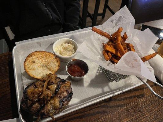 Burger with caramelized onions on a gluten free bun and sweet potato fries.