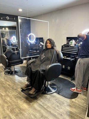 Customer with long hair in chair and super barber getting ready.