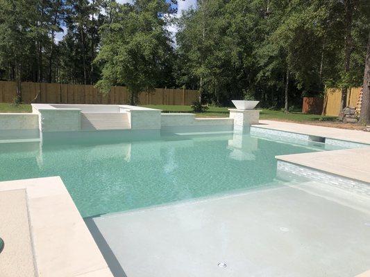 Pool with raised hot tub with split face stone waterfall with white quartz plaster finish