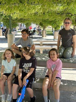 Kids sprawled on a picnic table in a lovely shaded area near the playground.